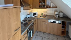 A compact kitchen with wooden cabinets, a microwave, a toaster, a stove, and a sink. - Apartment '4, Größe 60qm' with Balcony and Wi-Fi (Herscheid)