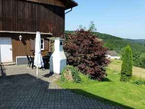 A rustic building with a chimney, outdoor seating, and a view of a green landscape.
