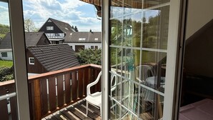 A room with a sliding glass door leading to a wooden deck with a white chair and a table. - Apartment '4, Größe 60qm' with Balcony and Wi-Fi (Herscheid)