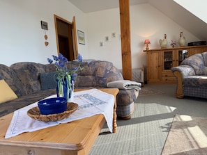 Ein gemütliches Wohnzimmer mit einer Couch, einem Holztisch, einem gemusterten Sessel und einem Schrank mit Dekoration.