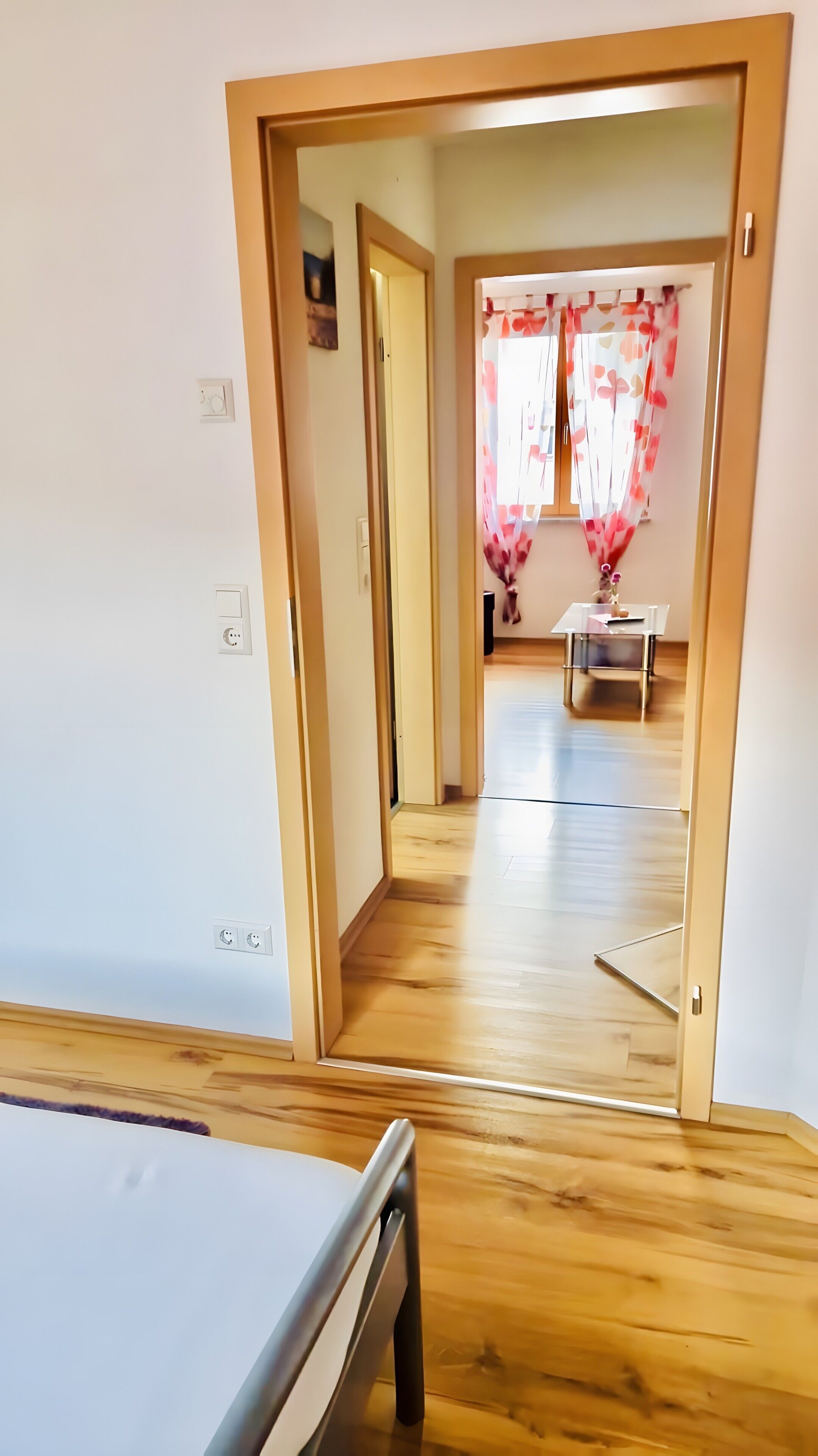 Un pasillo que conduce a una habitación con piso de madera, una mesa y una silla.