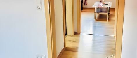 Un pasillo que conduce a una habitación con piso de madera, una mesa y una silla.