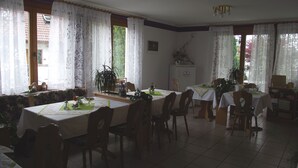 Ein Essbereich mit Tischen, Stühlen, einem Kühlschrank und einer Pflanze.