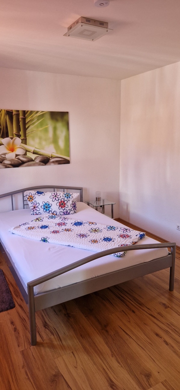 Ein Schlafzimmer mit einem Bett, einem Nachttisch, einer Wandlampe und einem Gemälde von Bambus und Blumen.