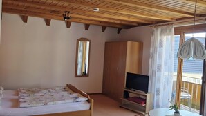 Un dormitorio con techo de madera, una cama, un televisor, un armario y un ventanal con cortinas.