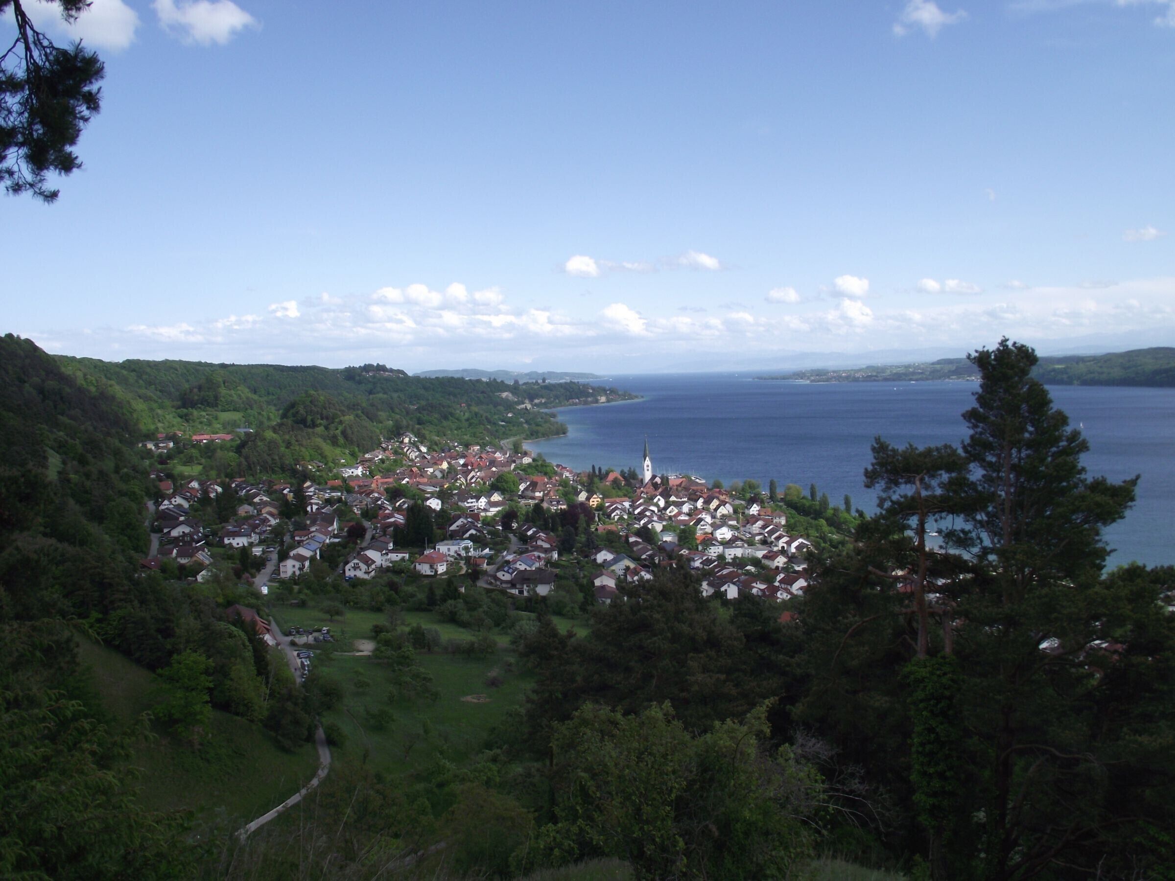 Une ville côtière avec une église, entourée de verdure et bordée d’une vaste étendue d’eau.