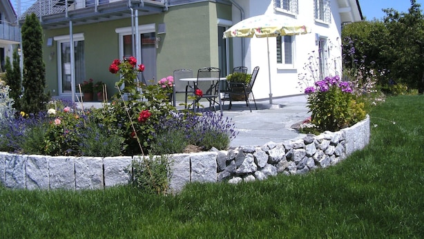 A two-story house with a balcony, outdoor seating, and a stone border.