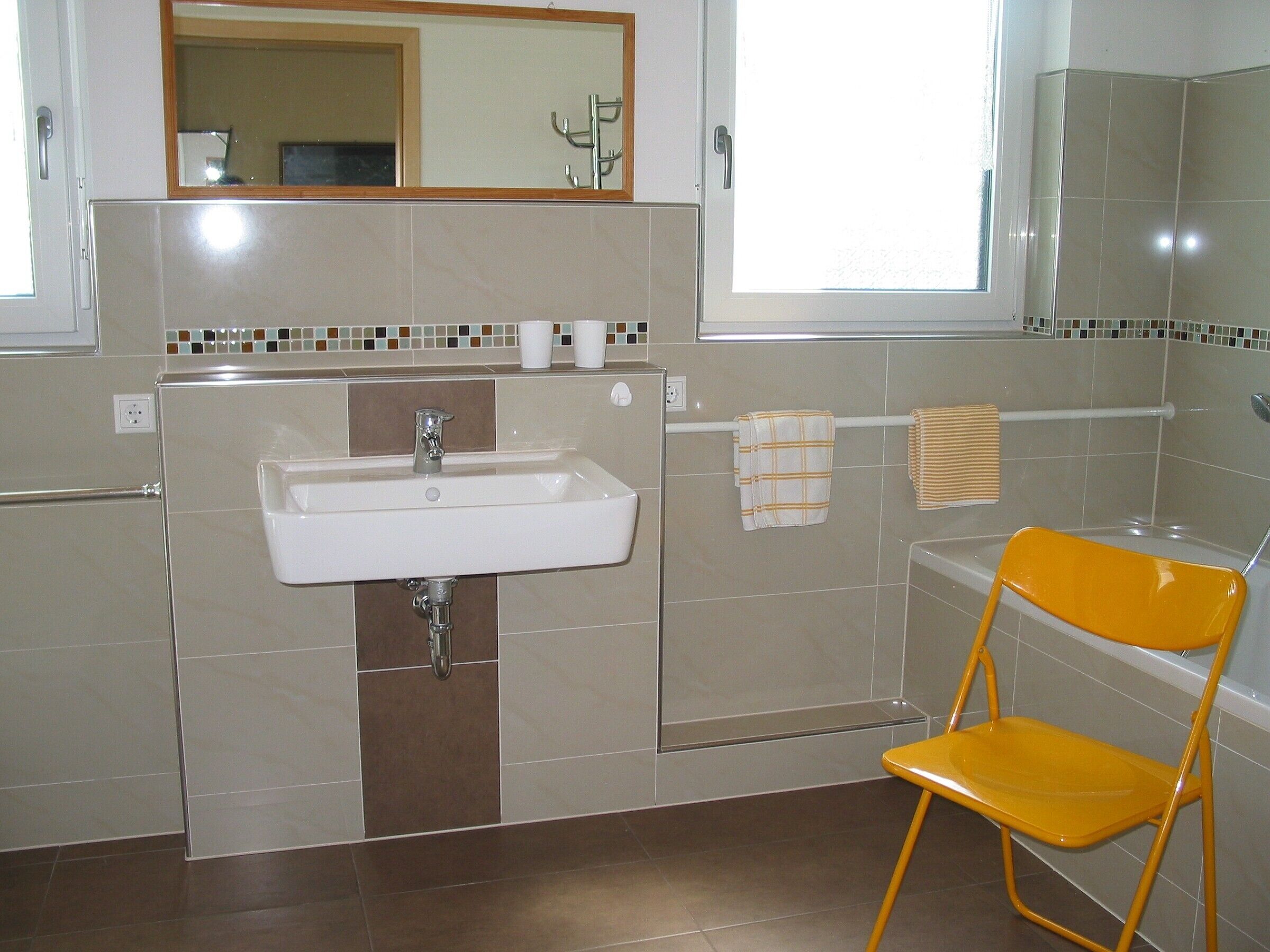 Un baño con lavabo, espejo, toallero y una silla amarilla.