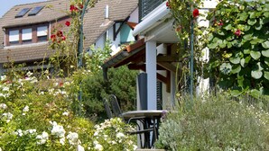 A garden with a bench, a chair, and a building with a sloped roof in the background. - Apartment 'Stapelfeldt' with Private Terrace, Shared Garden and Wi-Fi (Wasserburg (Bodensee))