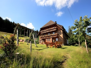 A wooden chalet with a balcony, surrounded by a grassy area and trees.