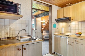 Une cuisine équipée d’un four encastré, d’un évier, de meubles de rangement en bois et d’un plan de travail sur lequel se trouve un saladier rempli de fruits.