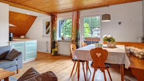 Una habitación acogedora con una mesa de comedor, sillas, un sofá, una zona de cocina y una ventana con cortinas.