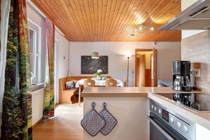 A modern kitchen with wooden ceiling, a dining area with a table and chairs, and a coffee machine.
