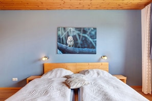 A bedroom with a bed, a wooden headboard, a wall-mounted picture of an owl, and bedside lamps.