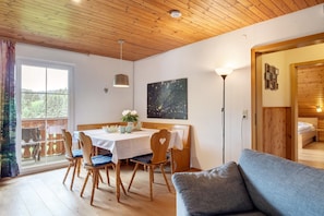 A room with a wooden ceiling, a dining table with chairs, a sofa, and a painting on the wall.