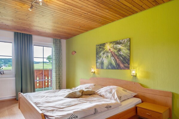 Une chambre avec un plafond en bois, un lit avec une literie blanche, une table de chevet, une lampe fixée au mur et une fenêtre avec des rideaux.