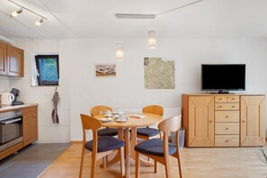 A modern kitchen with wooden cabinets, a dining table with chairs, a television, and a window with a view.