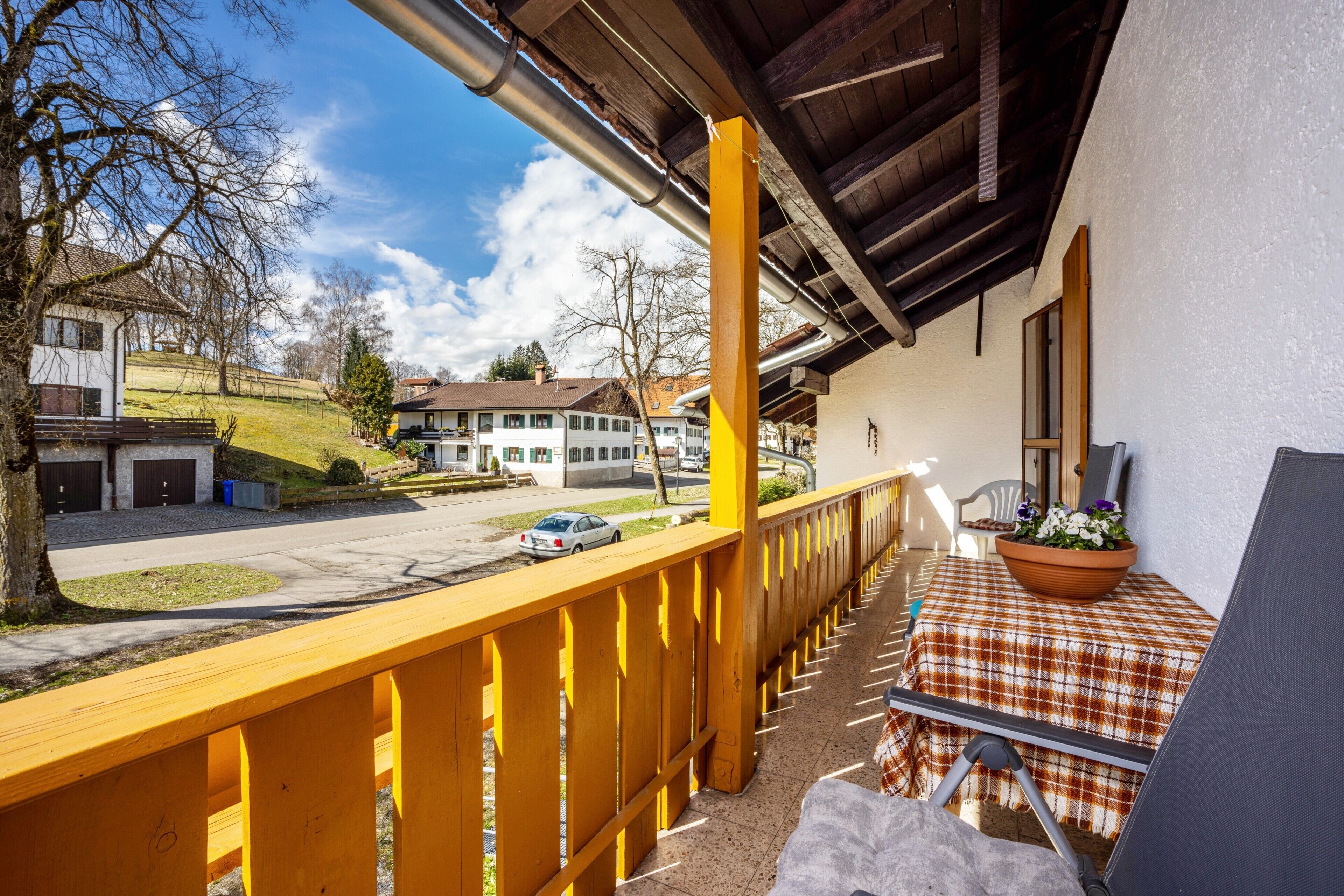 A balcony with a yellow railing, a checkered tablecloth, and a potted plant.