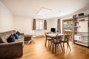 A living room with a sofa, a dining table with chairs, a TV, and a window with curtains.
