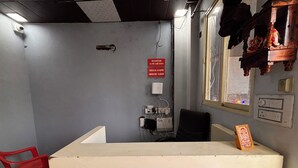 A reception desk with a red chair, a sign indicating check-in/out times, and a window with a view. - Dharohar Homestay (Rishikesh)