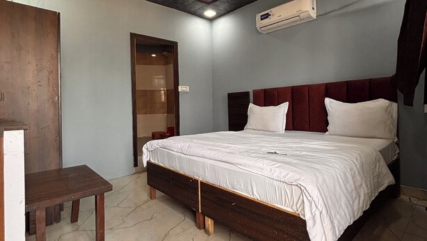 A bedroom with a bed, a wooden desk, a ceiling fan, and an air conditioning unit. - Dharohar Homestay (Rishikesh)