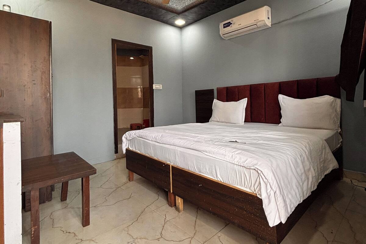 A bedroom with a bed, a wooden desk, a ceiling fan, and an air conditioning unit.