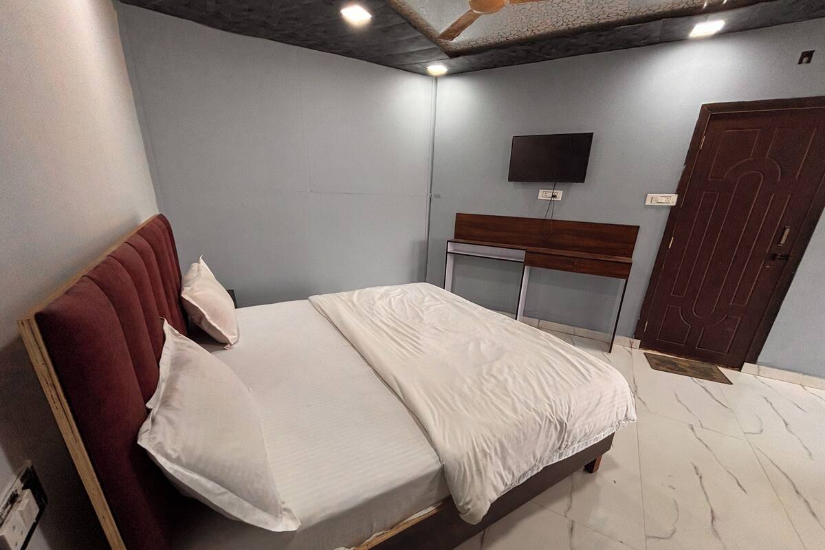 A bedroom with a bed, a wooden headboard, a flat-screen TV mounted on the wall, a wooden door, and a marble floor.