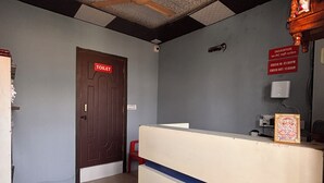 A reception area with a wooden door labeled "TOILET," a ceiling fan, and a sign indicating check-in and check-out times. - Dharohar Homestay (Rishikesh)