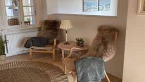 Tunnelmallinen nurkkaus, jossa on kaksi tuolia, pieni pöytä, lamppu ja ikkunasta avautuva näkymä merelle.