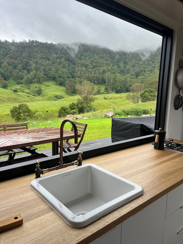 A kitchen with a view of a green landscape and mountains.