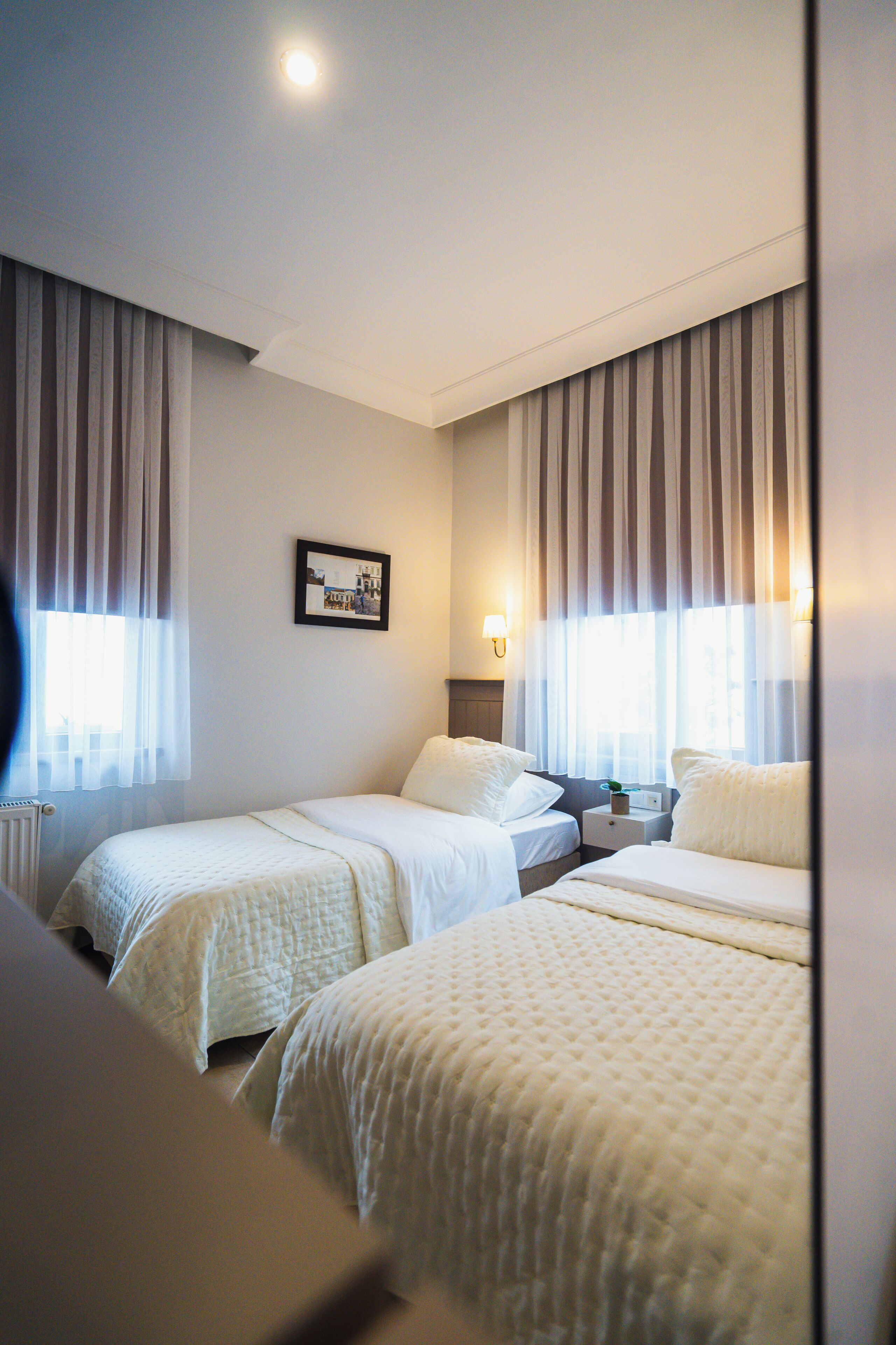 A hotel room with two beds, a nightstand, a framed picture on the wall, and curtains on the windows.