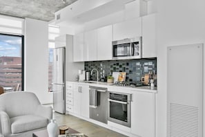 A modern kitchen with white cabinets, a stainless steel refrigerator, a microwave, and a tiled backsplash. - Calgary Tower View | King Bed | Mins to Saddledome (Calgary)