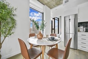 A modern kitchen with a stainless steel refrigerator, a dining table with chairs, and a view of the cityscape through large windows. - Calgary Tower View | King Bed | Mins to Saddledome (Calgary)