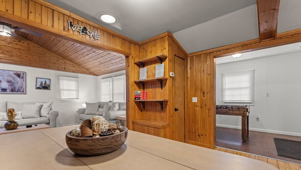 A cozy living room with a wooden ceiling, a sofa set, a coffee table with a decorative bowl, and a foosball table.
