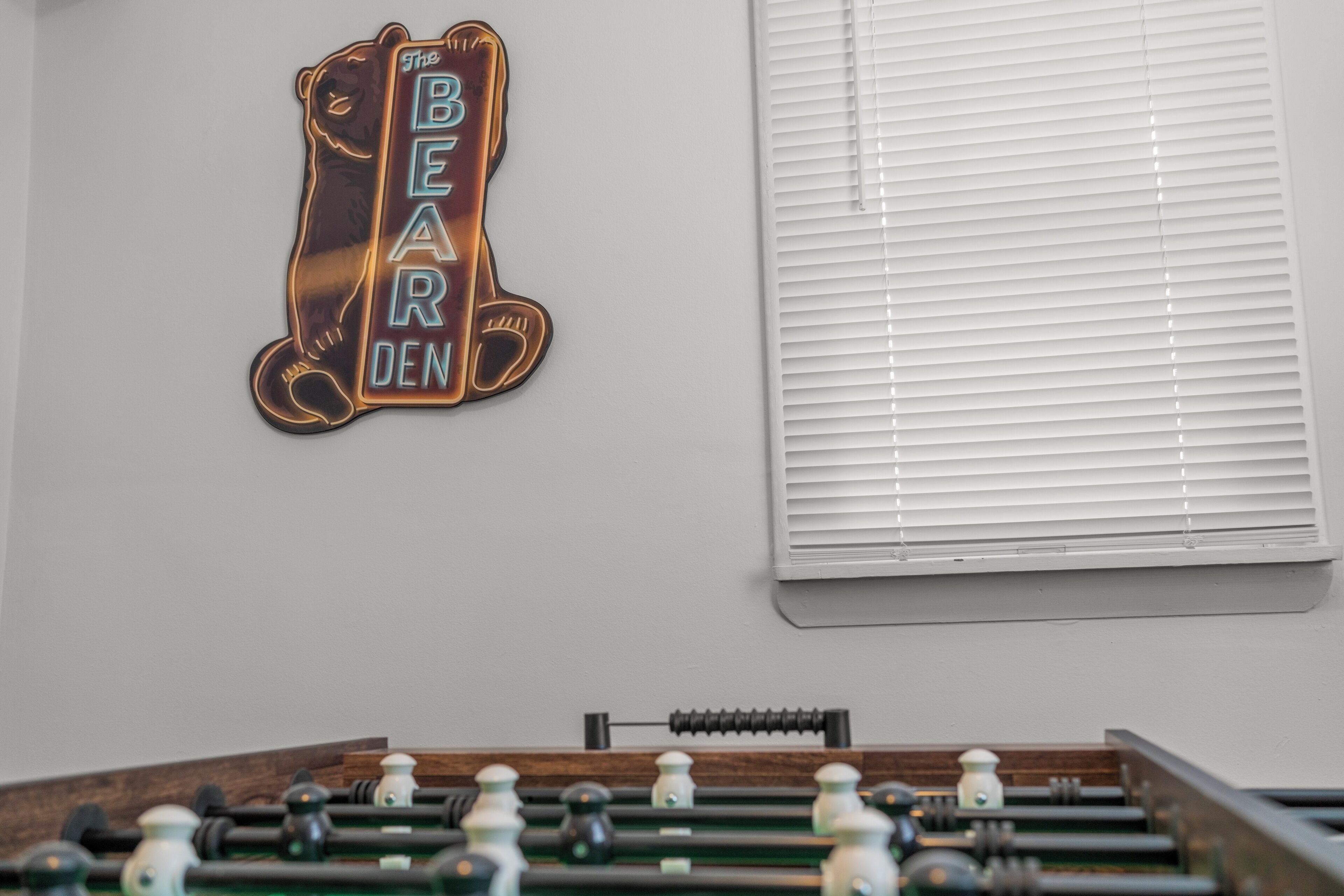 Un tavolo da calcio in una stanza con un cartello appeso al muro che recita 'This BAR DEN'.