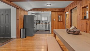 A kitchen with wooden walls, a grey door, and a stainless steel refrigerator.