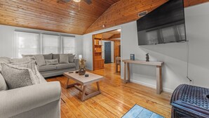 A spacious living room with a wooden ceiling, a sofa, a coffee table, and a TV mounted on the wall.