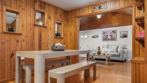 A wooden interior with a dining table, benches, a sofa, and a wall with framed pictures.