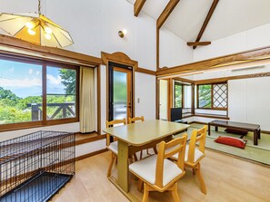 Una habitación con una mesa de madera, sillas, un televisor y ventanas grandes con vistas a zonas verdes.