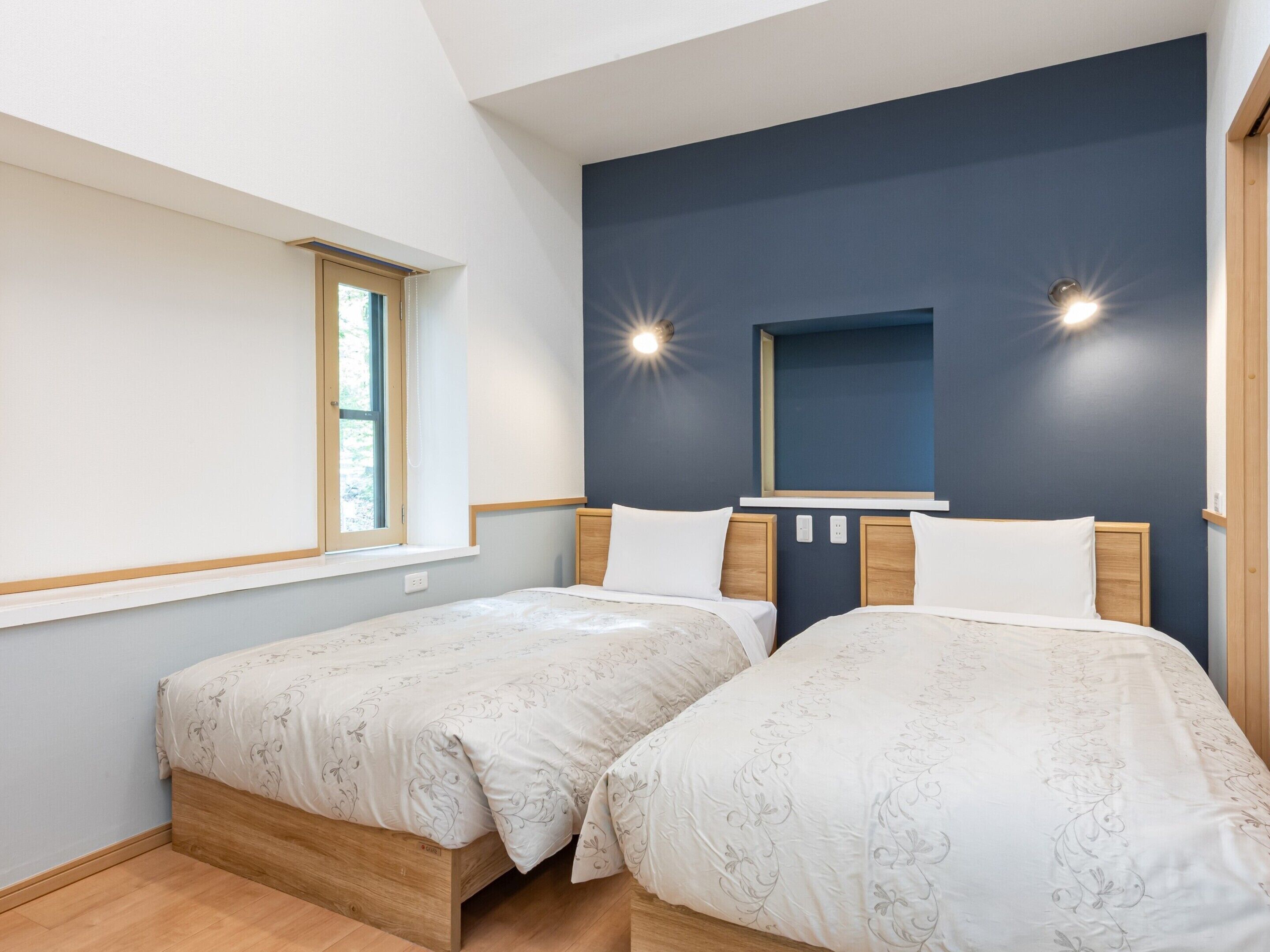 Une chambre avec deux lits, une fenêtre et des lampes fixées au mur.