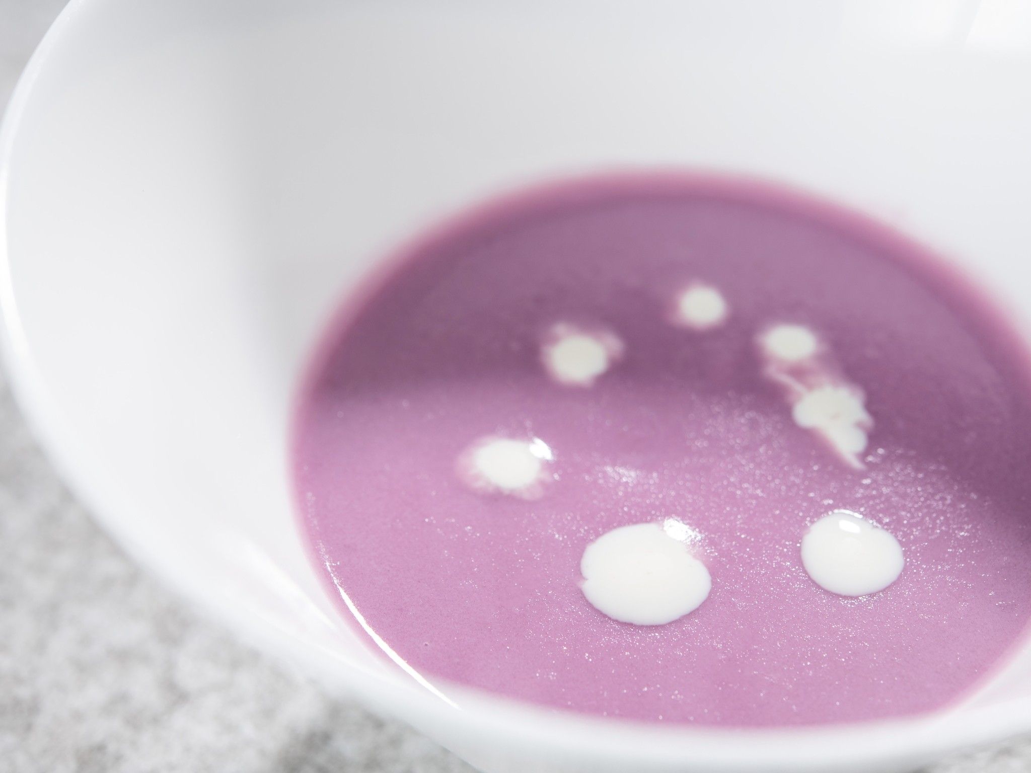 Un bol blanc contenant une substance violette et de petites gouttes blanches.