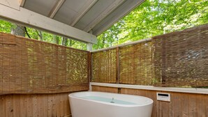 Un espace de détente en bois comprenant une grande baignoire blanche, des paravents en bambou pour plus d’intimité et une terrasse en bois.