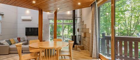 Ein modernes Interieur mit Holzbalkendecke, einem runden Esstisch mit Stühlen, einer Couch und einem Fernseher.