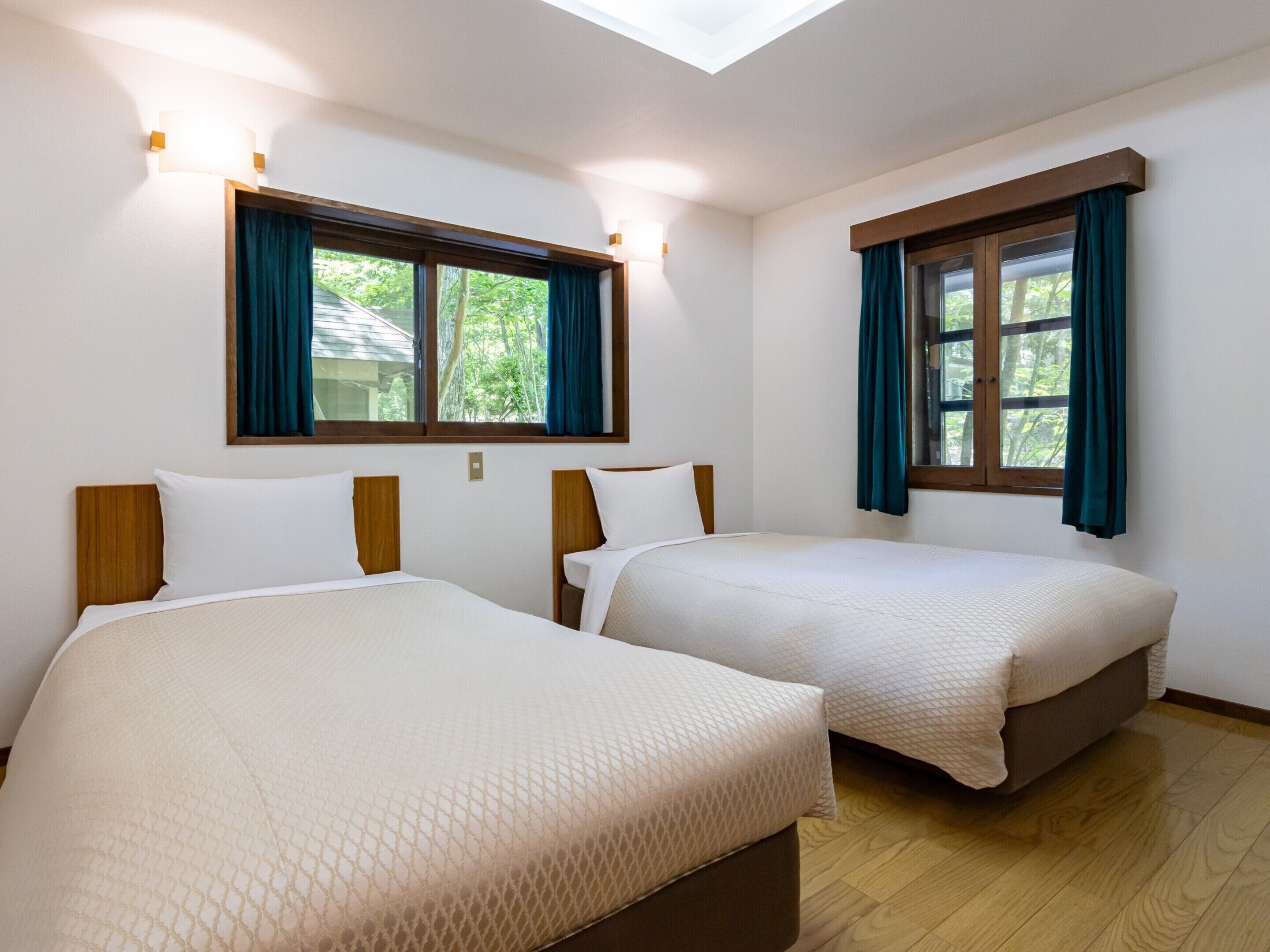 A room with two beds, a skylight, and windows with curtains.