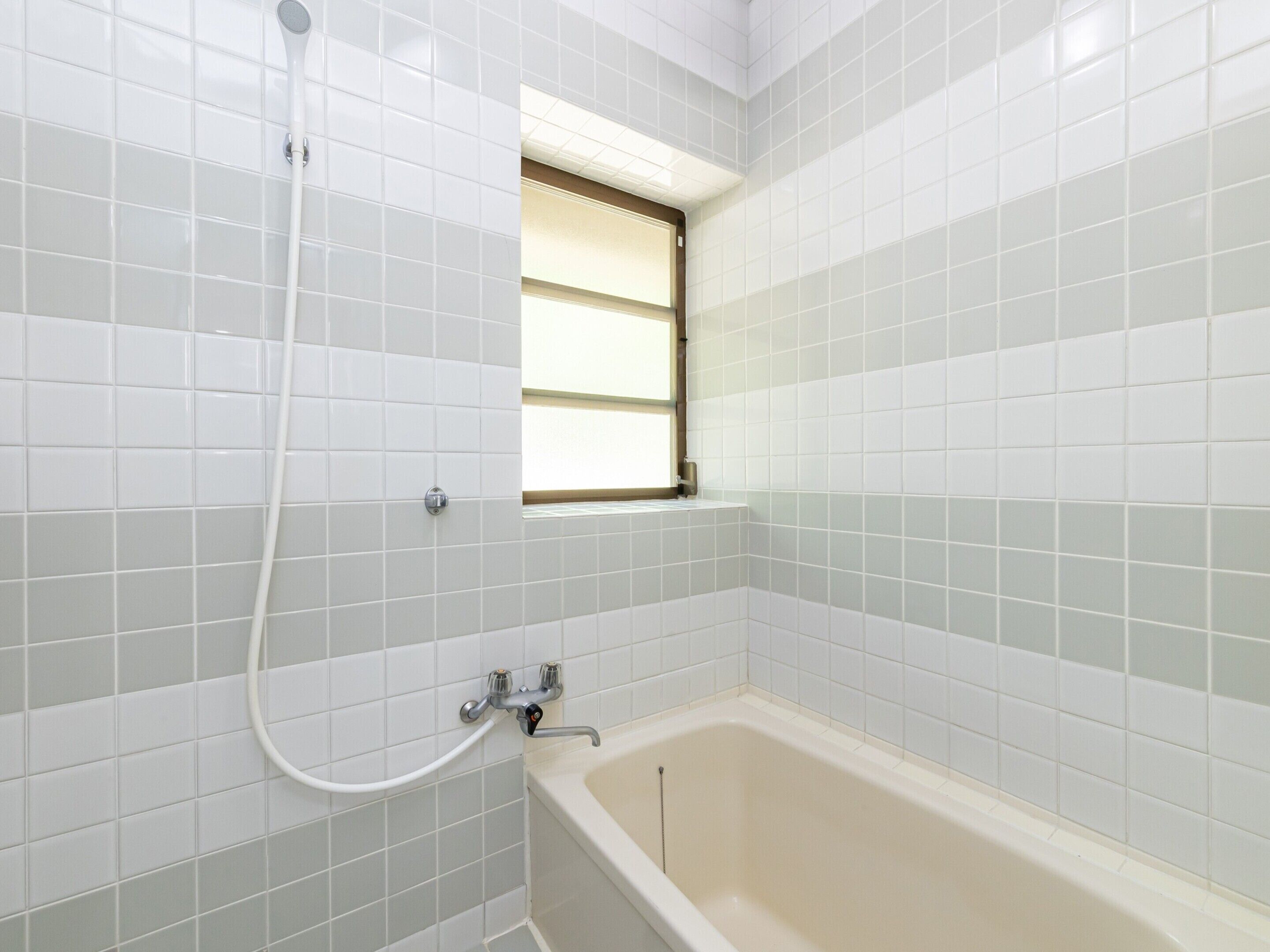 A bathroom with white tiles, a bathtub, a shower, and a window.