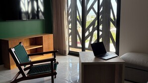 Un salon moderne avec un mur d’accent vert, un téléviseur à écran plat, une chaise en bois, une petite table avec un ordinateur portable et une grande fenêtre donnant sur des immeubles.
