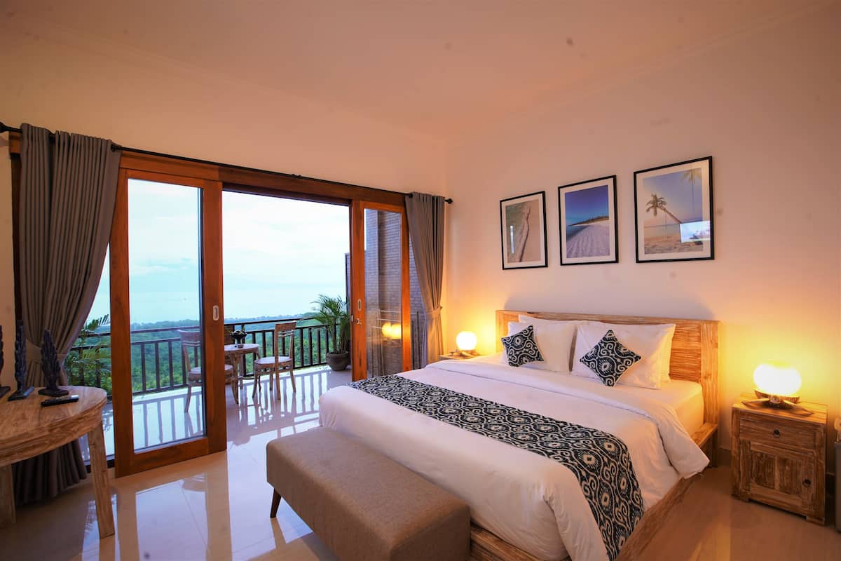 A bedroom with a large bed, a balcony, and three framed pictures on the wall.