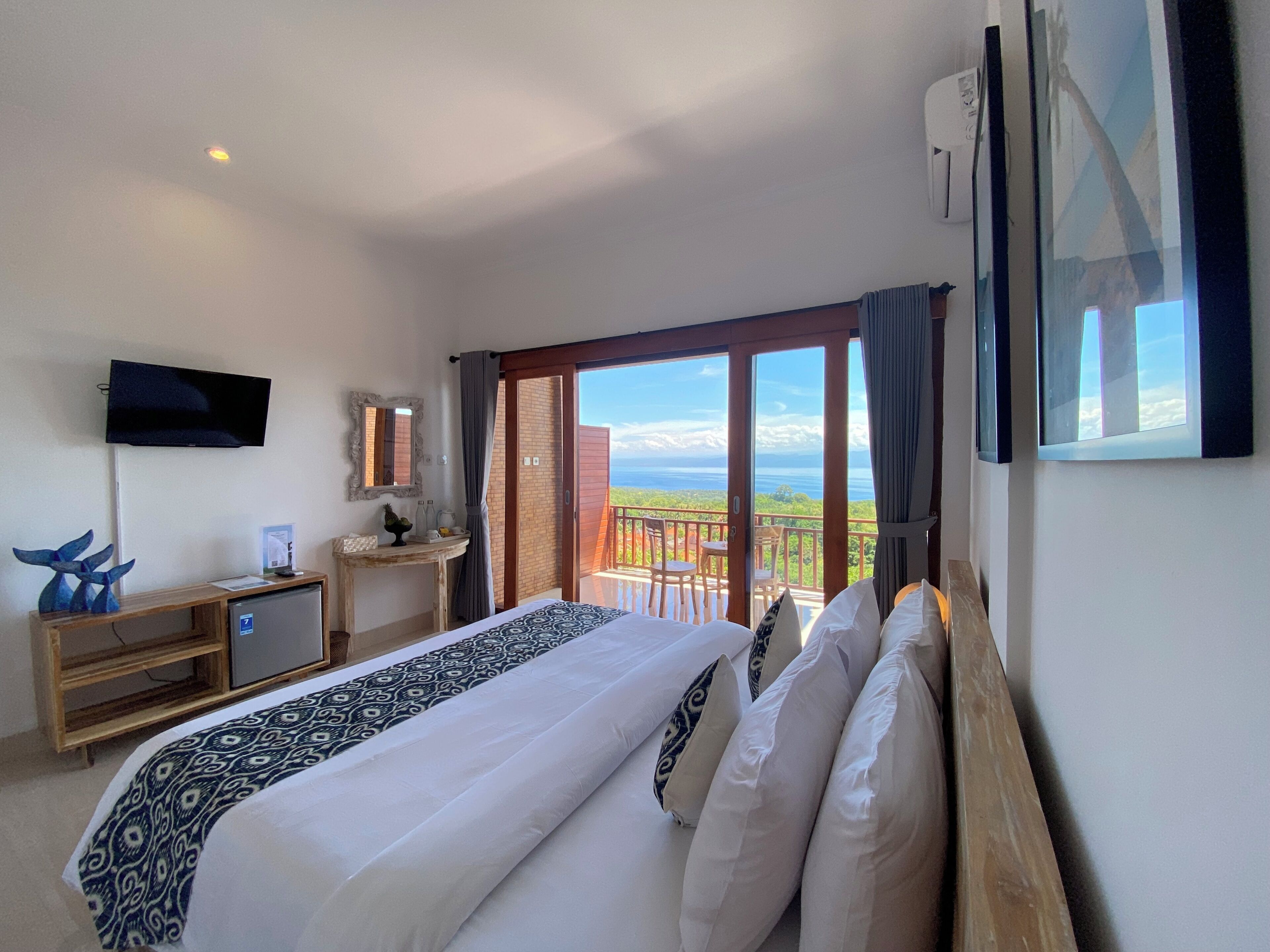 A hotel room with a bed, a TV, a desk, a small table, and a balcony with a view.