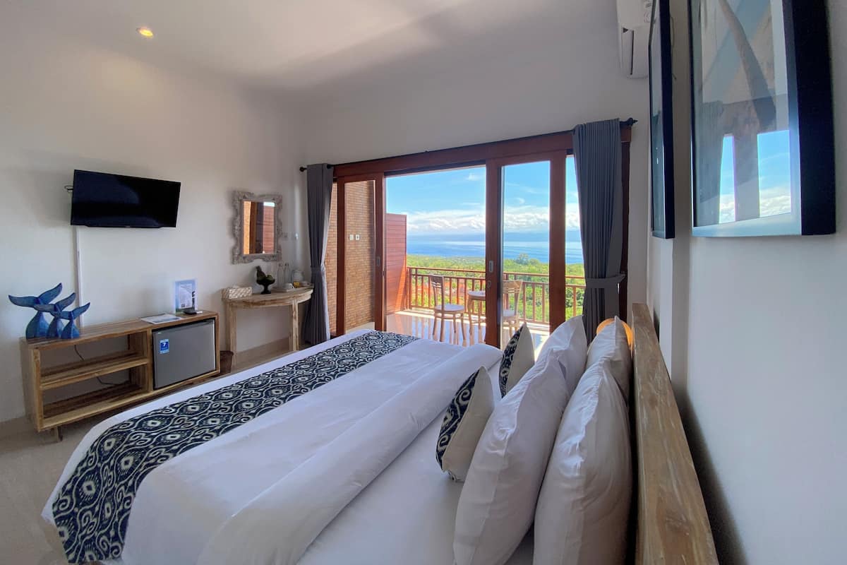A hotel room with a bed, a TV, a desk, a small table, and a balcony with a view.