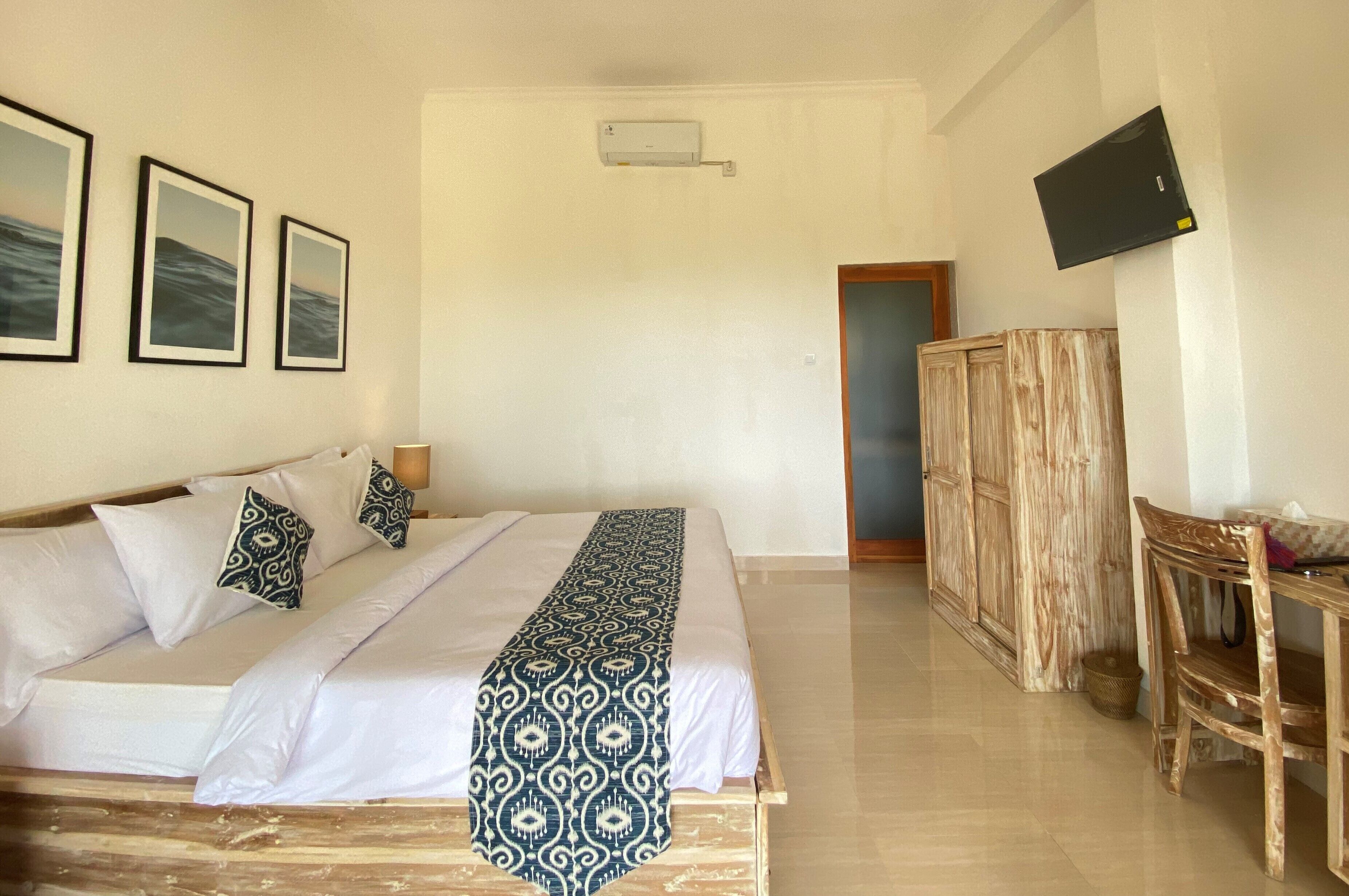 A hotel room with a bed, a TV mounted on the wall, and a wooden wardrobe.